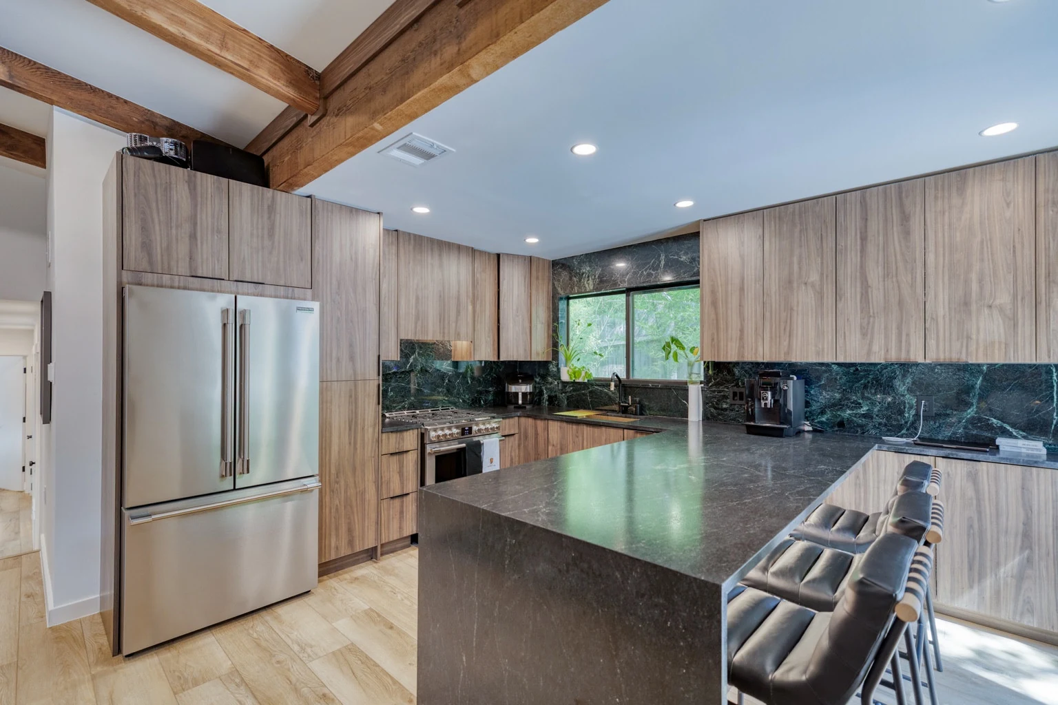 Modern walnut kitchen with honed Black Mist countertops, a waterfall end panel and a Verde Alpi marble window surround